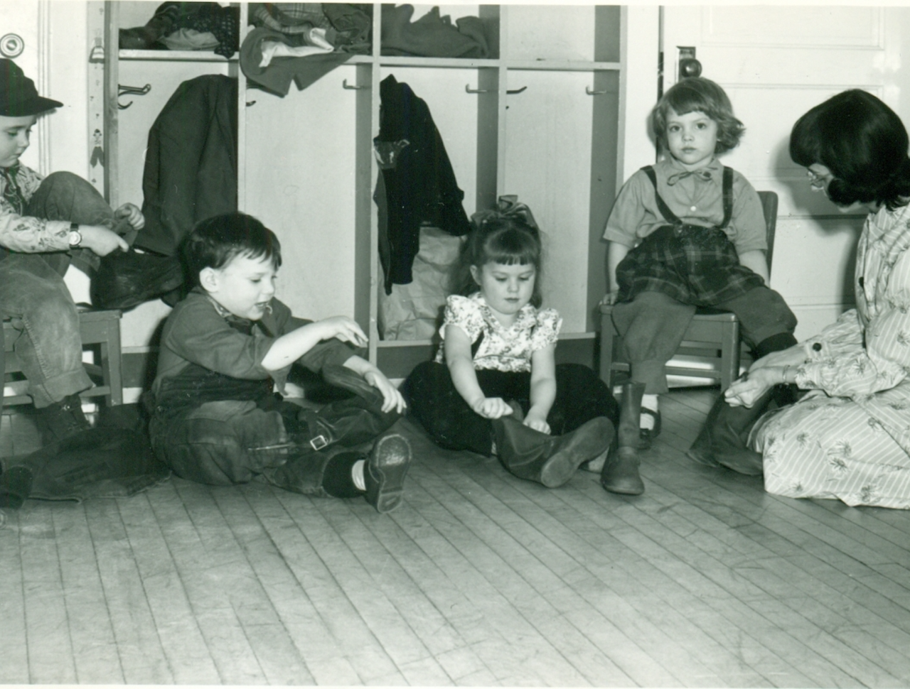 Black and white photo of children putting on shoes.